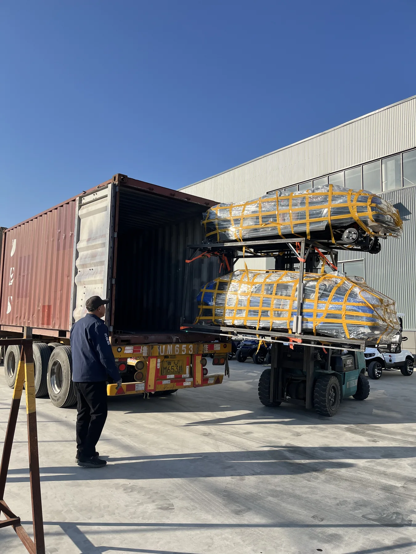 A forklift positioning framed, wrapped vehicles at an open shipping container
