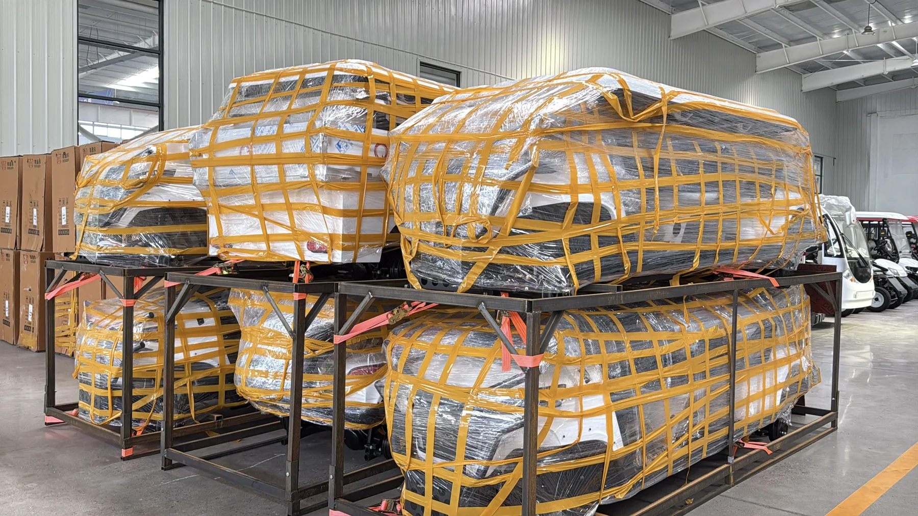 Wrapped golf carts arranged in metal shipping frames inside the workshop